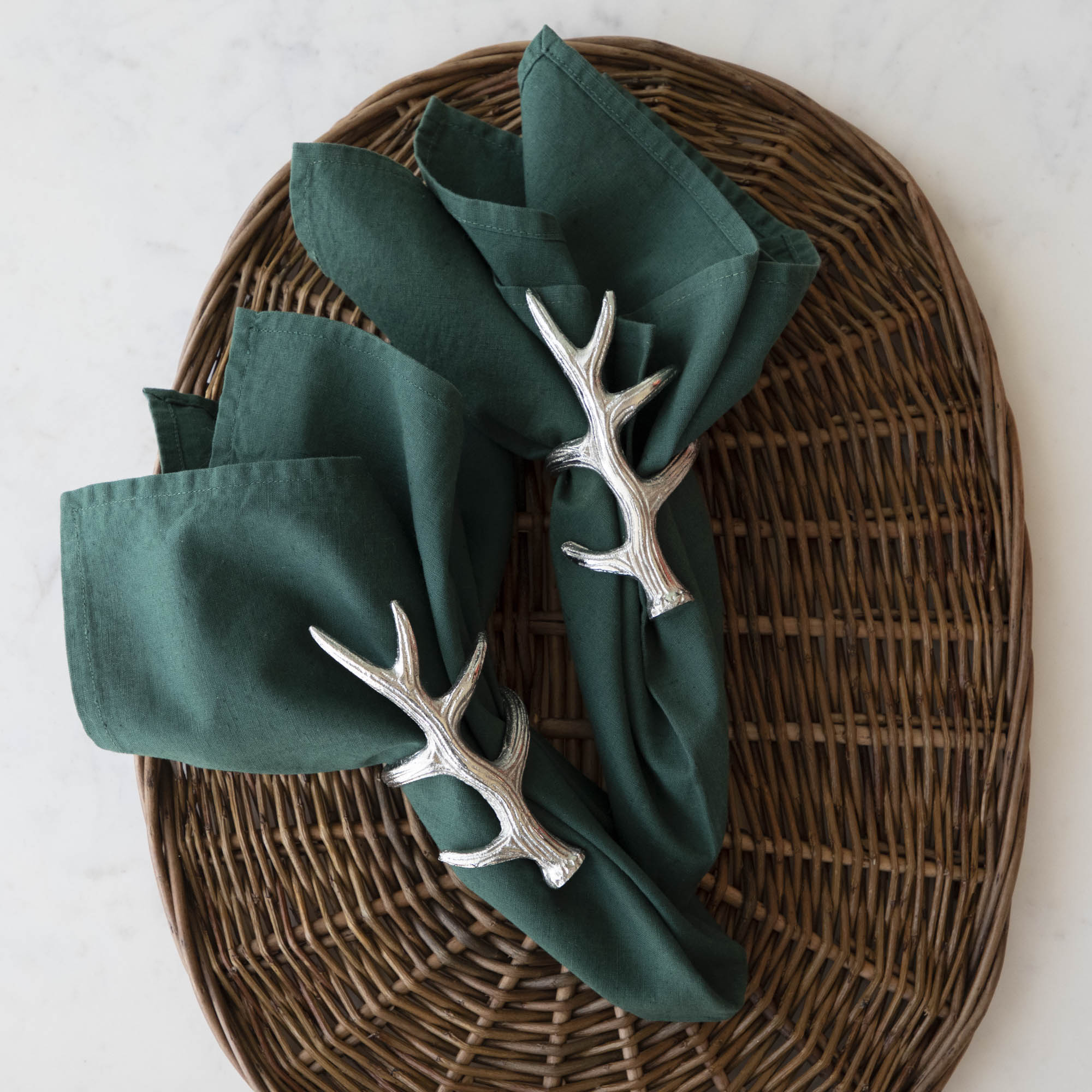 A napkin ring featuring an antler design, placed on a woven background with a green napkin inserted.