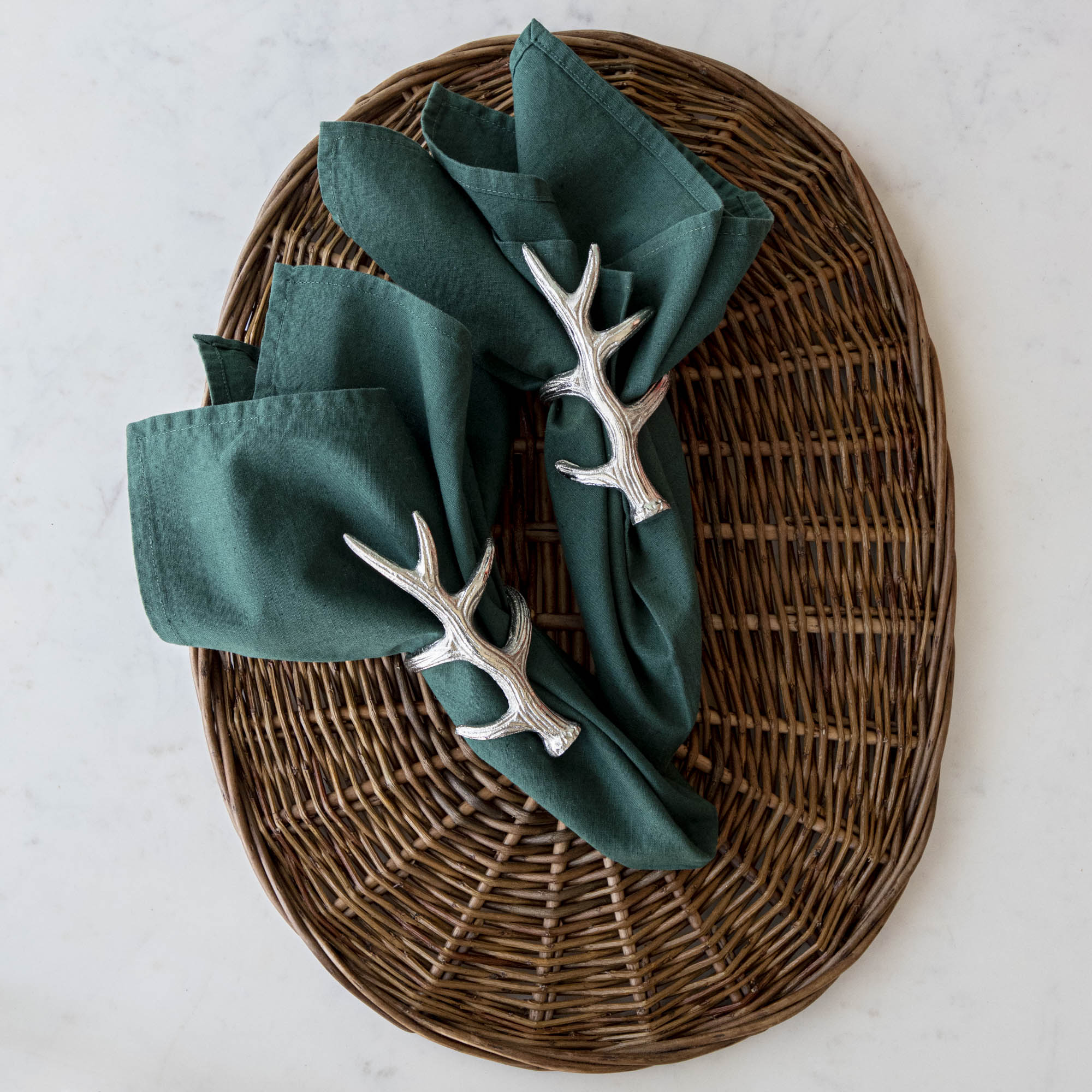 A napkin ring featuring an antler design, placed on a woven background with a green napkin inserted.