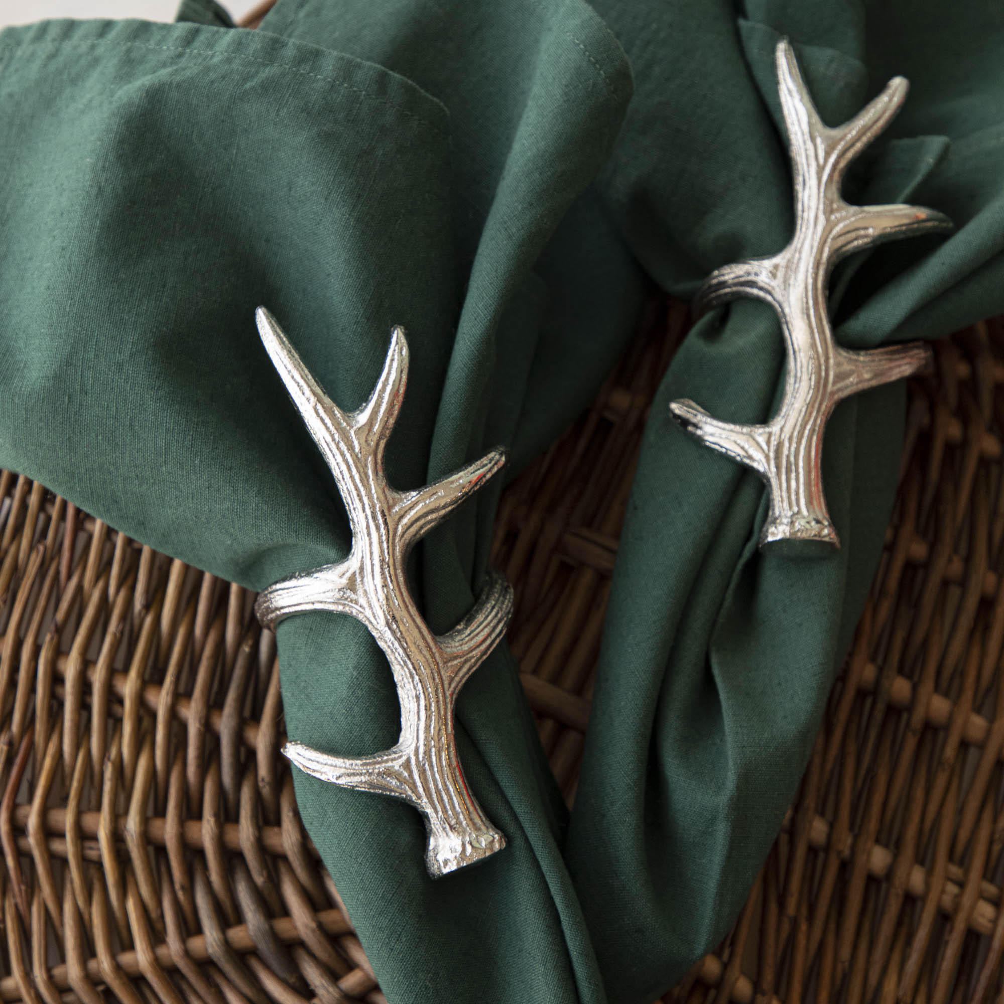A napkin ring featuring an antler design, placed on a woven mat, with a green napkin inserted.