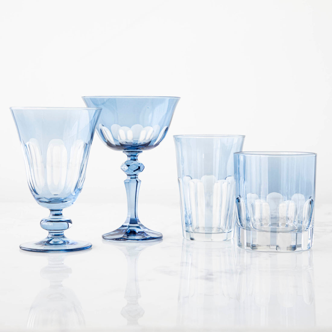 A set of four Rialto Thistle (Light Blue) Glasses by SIR/MADAM on a reflective surface.