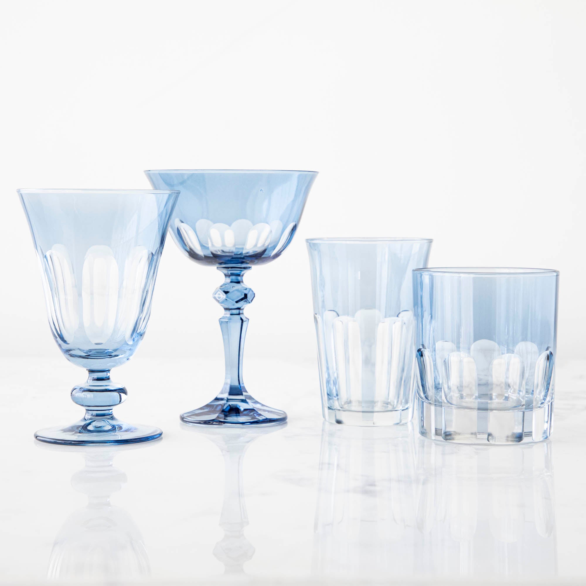 A set of four Rialto Thistle (Light Blue) Glasses by SIR/MADAM on a reflective surface.