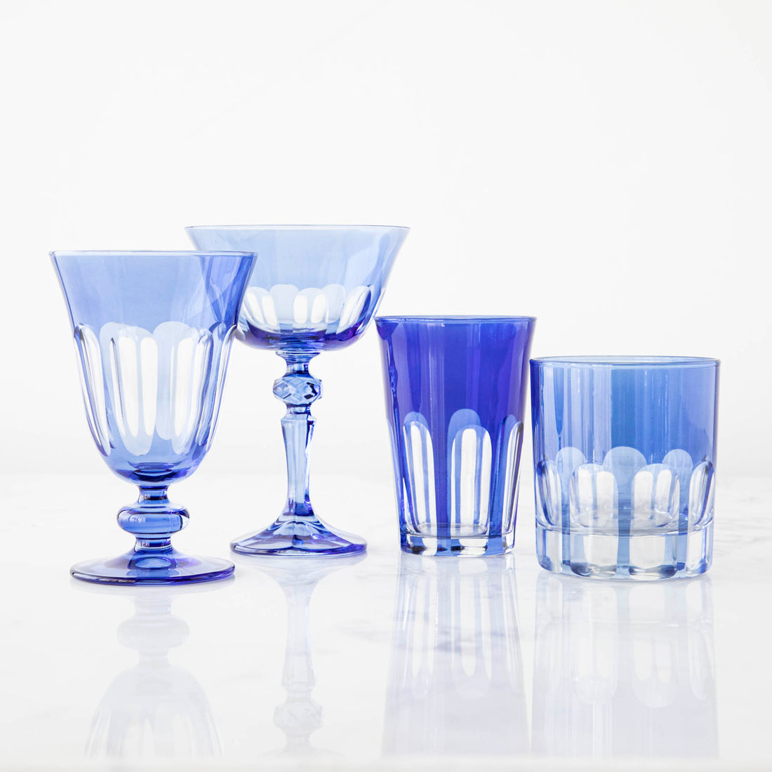 A set of blue Rialto Moon Glow Glasses by SIR/MADAM on a reflective surface.