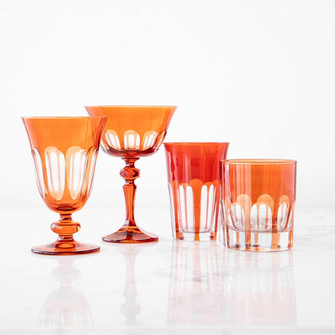 A collection of four dark red Rialto Lolita Glasses by SIR/MADAM on a reflective surface.