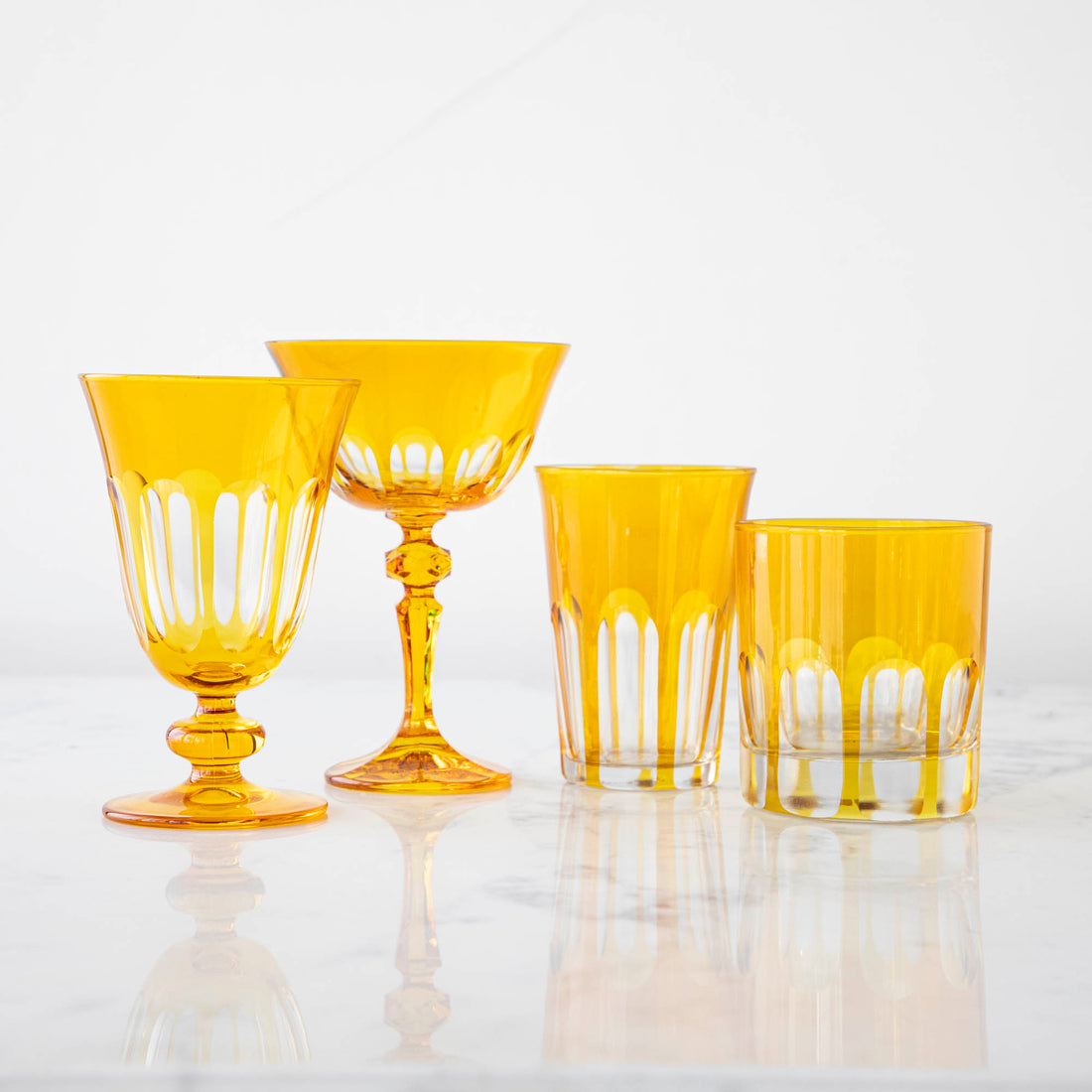 A set of Rialto Ginger (Dark Yellow) glasses from SIR/MADAM on a white surface, including two stemmed glasses and two tumblers with a vertical line pattern.