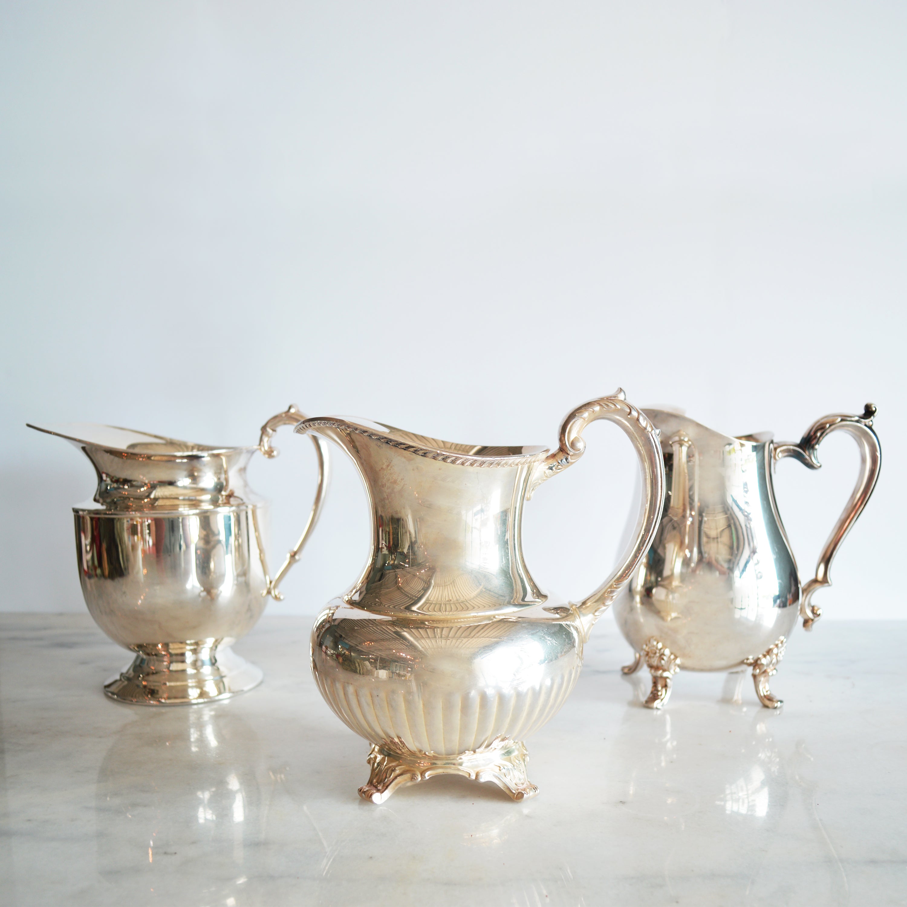 Elegant Hester & Cook vintage silver-plate water pitcher on a table adorned with glasses, plates, and a potted fern in the background.