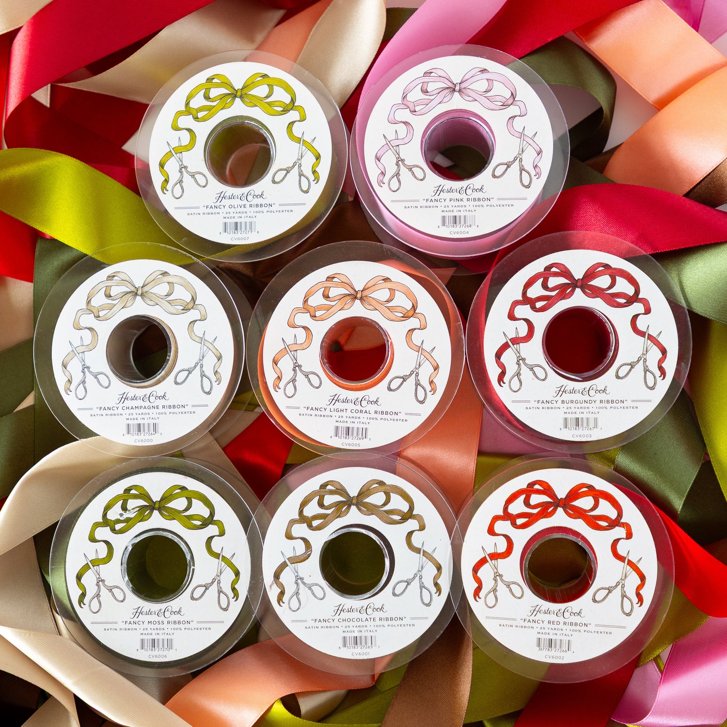 Colorful spools of ribbon in rows, on top of a pile of colorful ribbons intertwined.