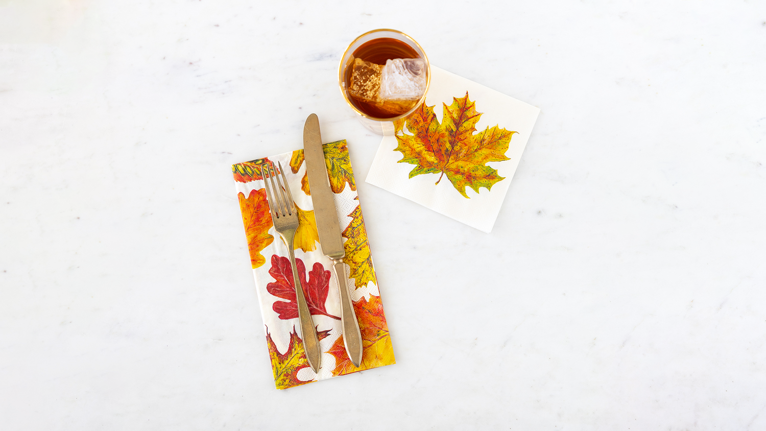 Hester &amp; Cook Fall Foliage Cocktail &amp; Guest Napkins on a marble table with a fork and knife and glass of iced tea.