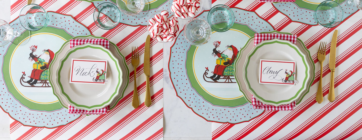 A Christmas themed table setting featuring the Die-cut Old St. Nick Sleigh Placemats, Green Icing on the Cake plates, Old St. Nick Sleigh Place Cards and gold flatware on the Peppermint Stripe Runner.