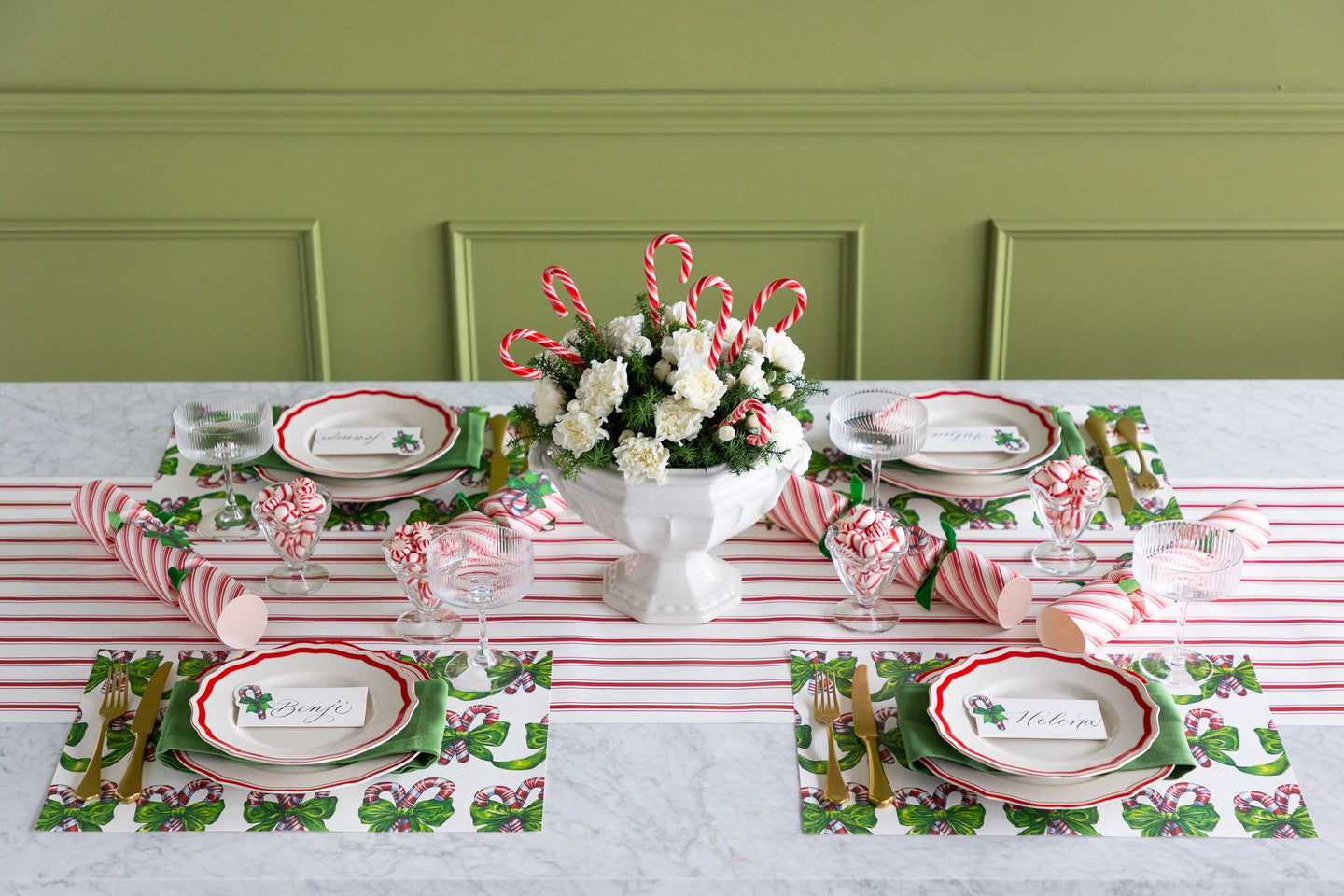 Table set with festive holiday placemats with a centerpiece that has flowers and candy canes in it. 