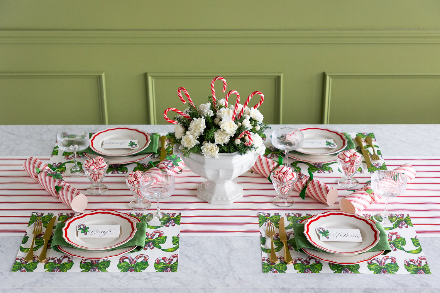 Table set with festive holiday placemats with a centerpiece that has flowers and candy canes in it. 