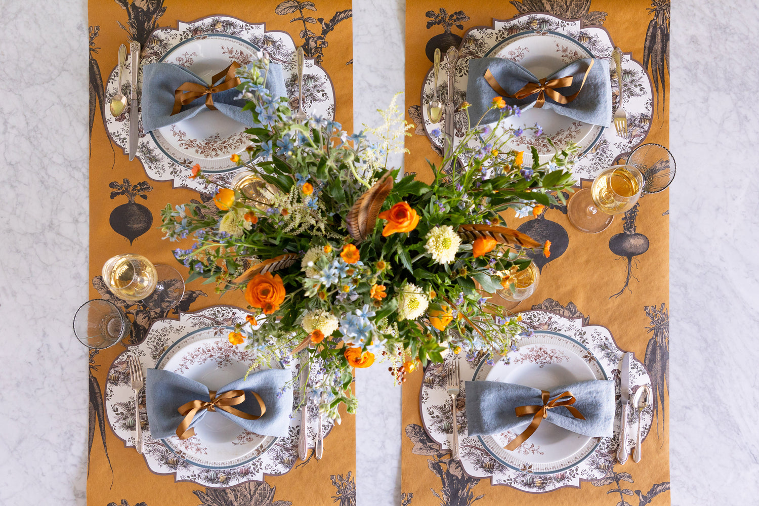 Decorative table setting with floral centerpiece, plates, and gold accents on a patterned table runner.