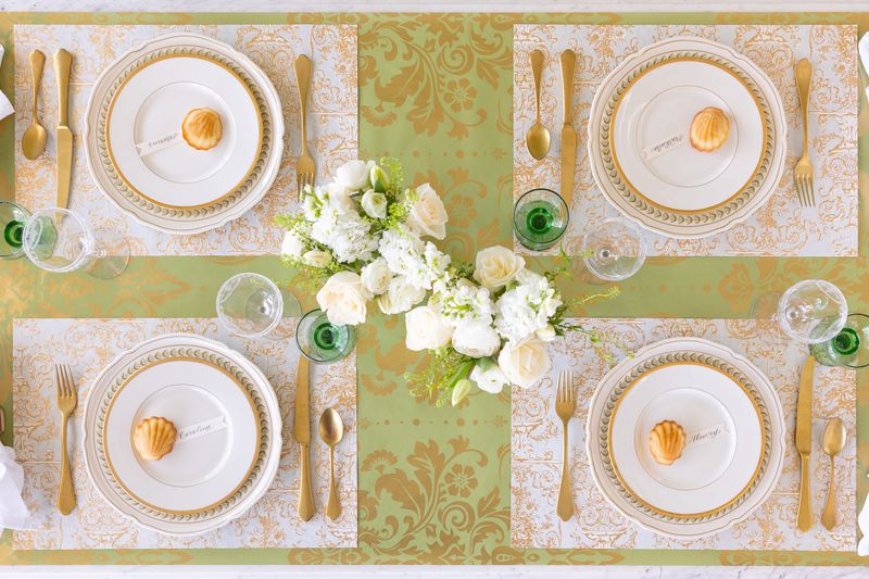 Elegant table setting featuring the Gilded Scroll placemats on a green runner with plates and gold cutlery laid out. 