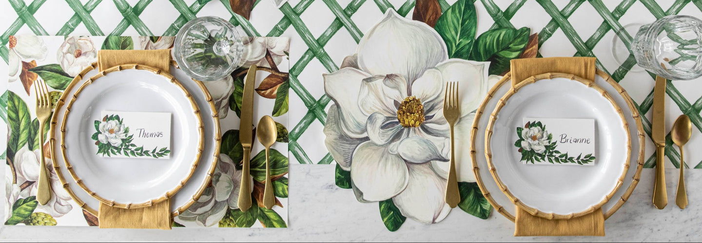 A table set for four with the Die-cut Magnolia and Magnolia Blooms Placemats, bamboo dinnerware, gold flatware and Magnolia Place Card on the Green Lattice Runner.