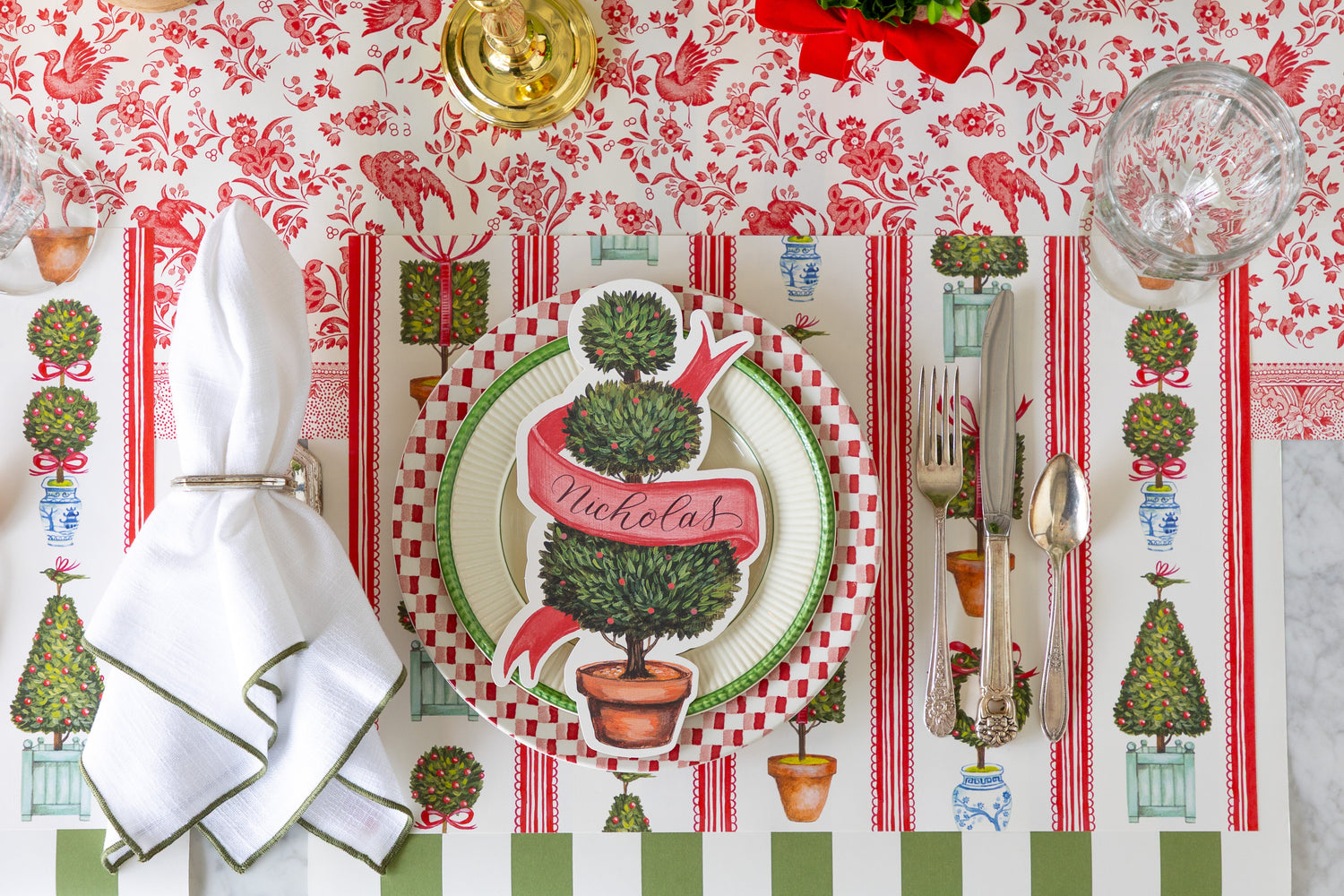 A festive table setting featuring the Holiday Topiary Placemat, vintage plates and silverware and Holiday Topiary Table Accent on the Moss Classic Stripe and Red Regal Peacock Runner.