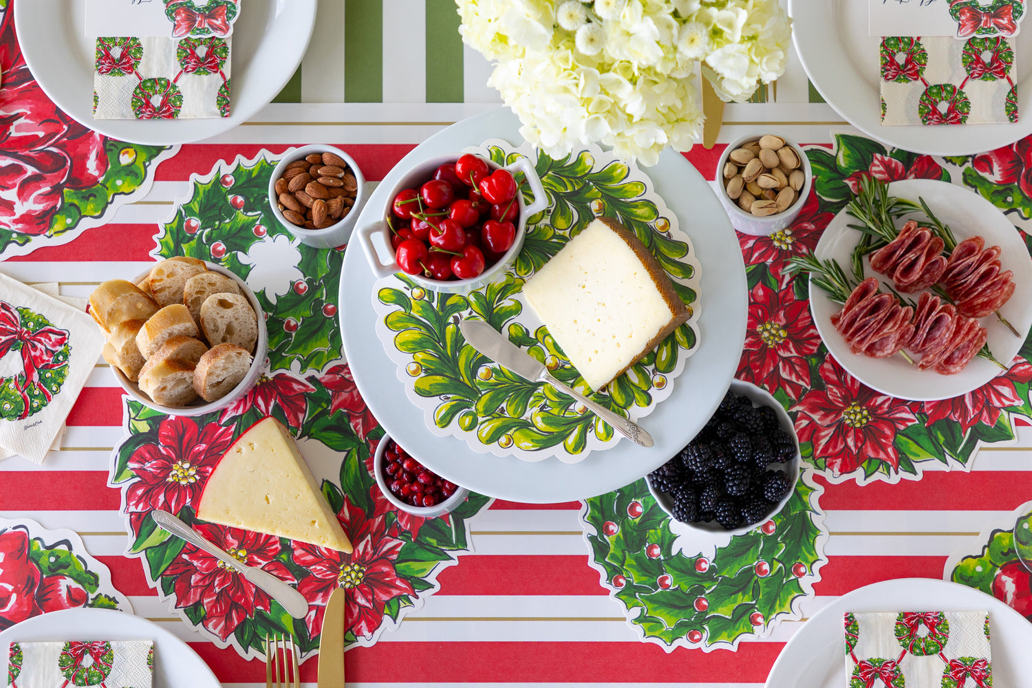 A Christmas table setting featuring the Holiday Wreath Serving Papers with various fruit, nuts cheeses and bread.