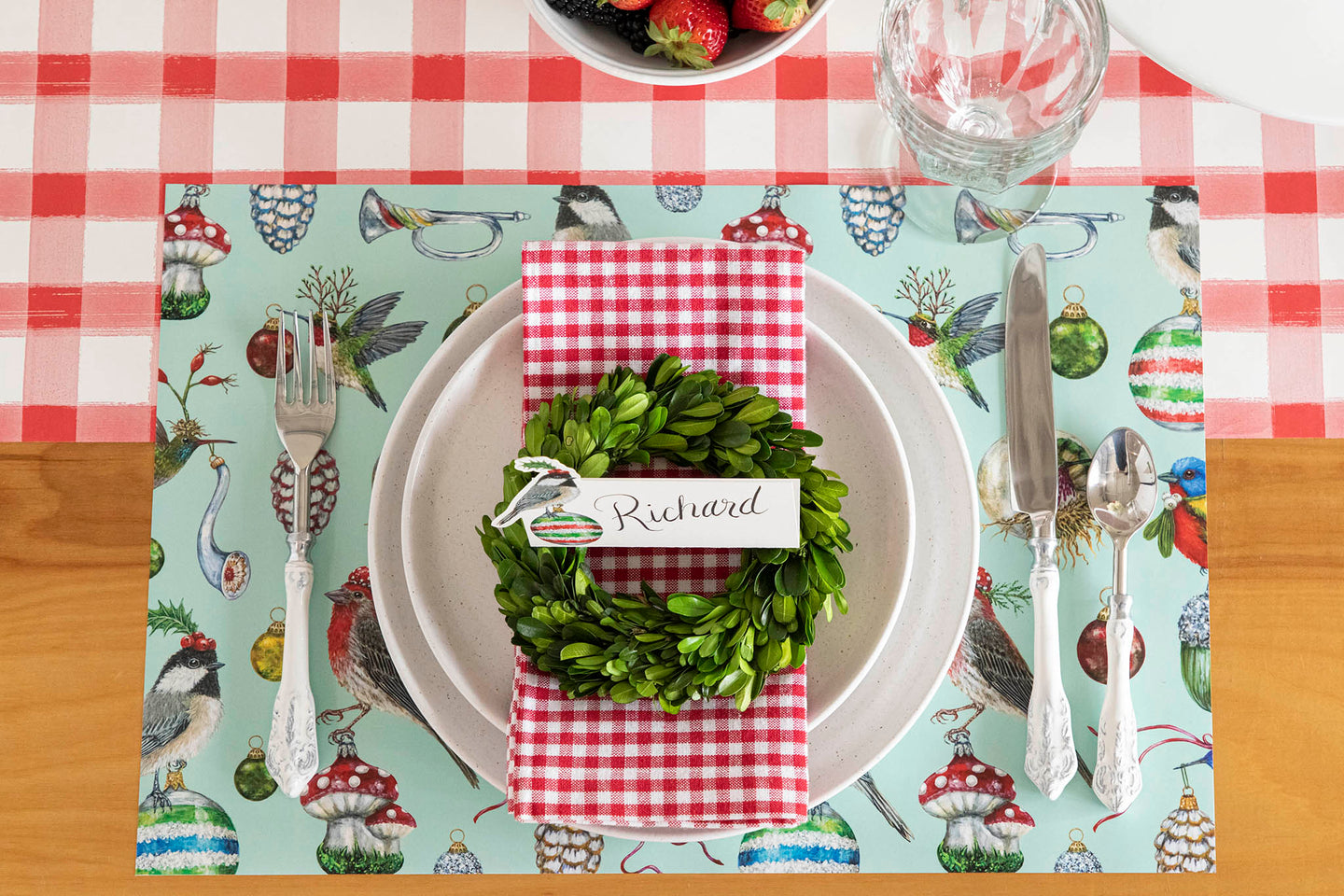A Christmas place setting featuring the Baubles & Birsd Placemat, a topiary wreath and Christmas Chickadee Place Card on the Red Painted Check Runner.