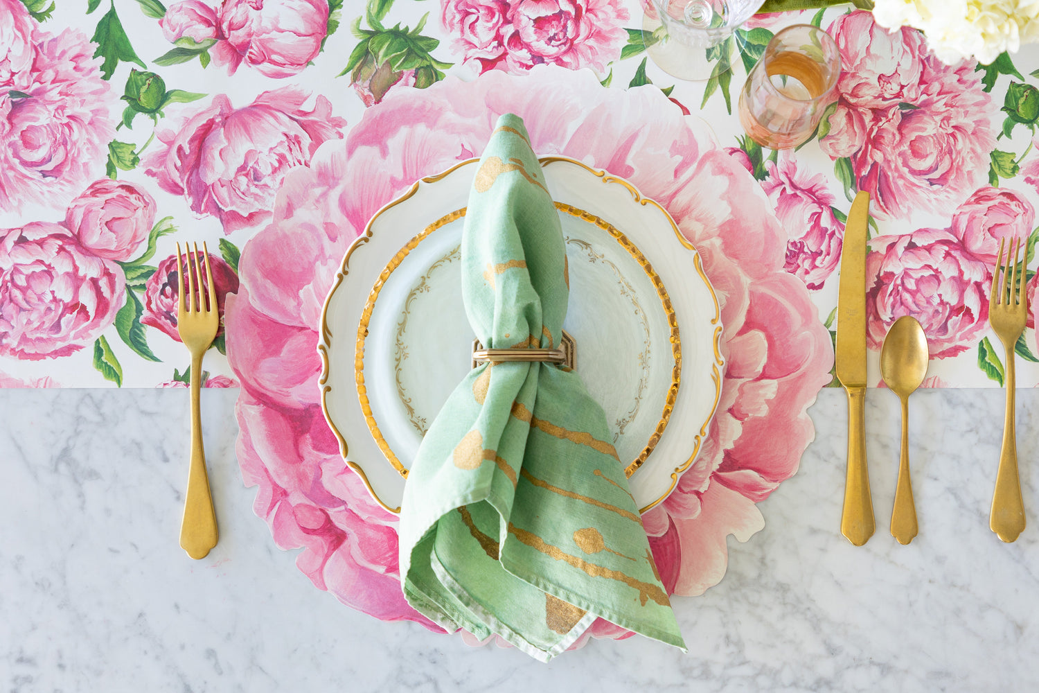 A place setting with the Die-cut Peony Placemat, decorative plates, marbled napkin and gold flatware on the Peonies in Bloom Runner.