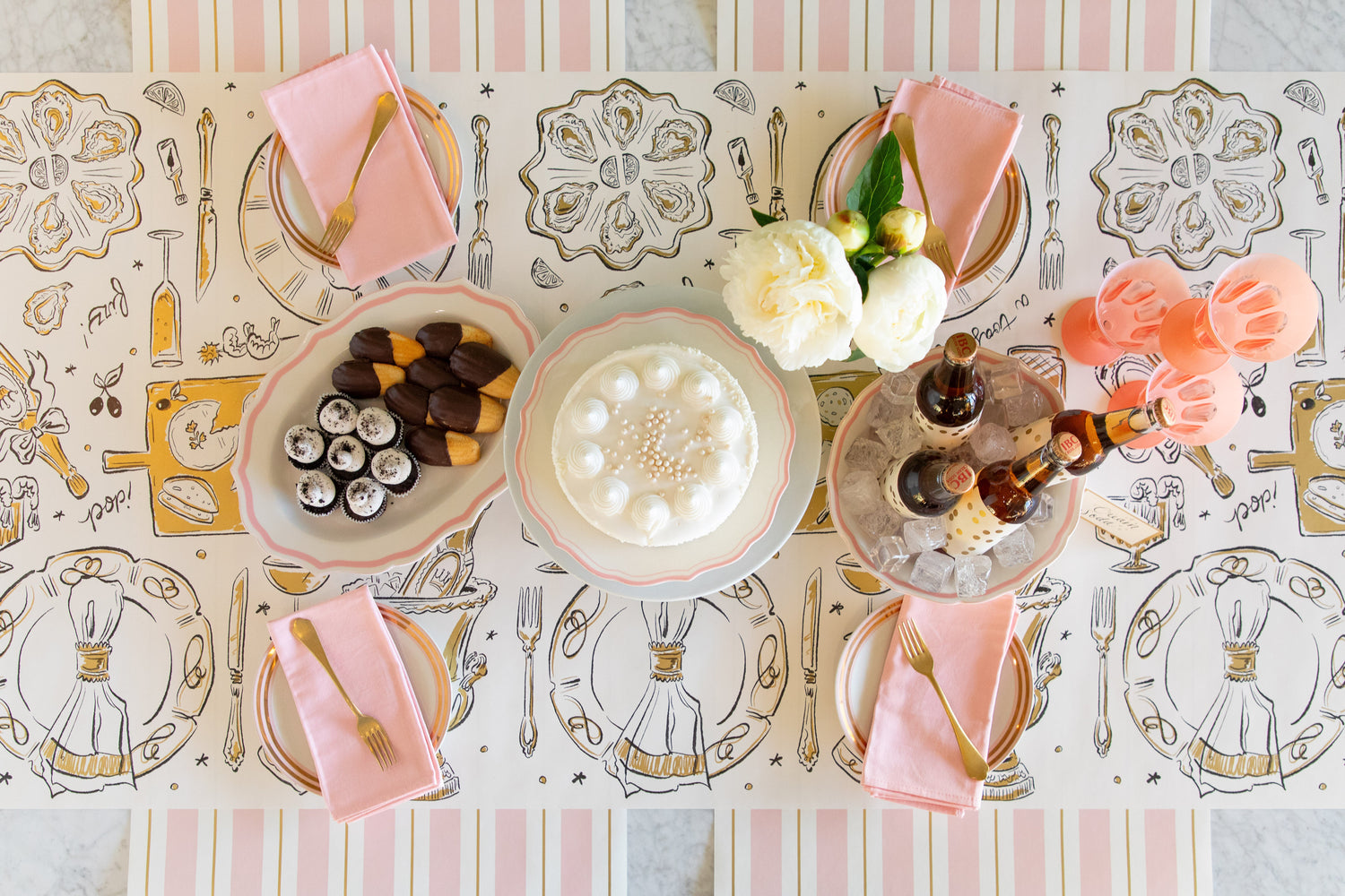 A celebratory table setting featuring the Cocktail Party Runner, gold, pink and white dinnerware and various treats and drinks.