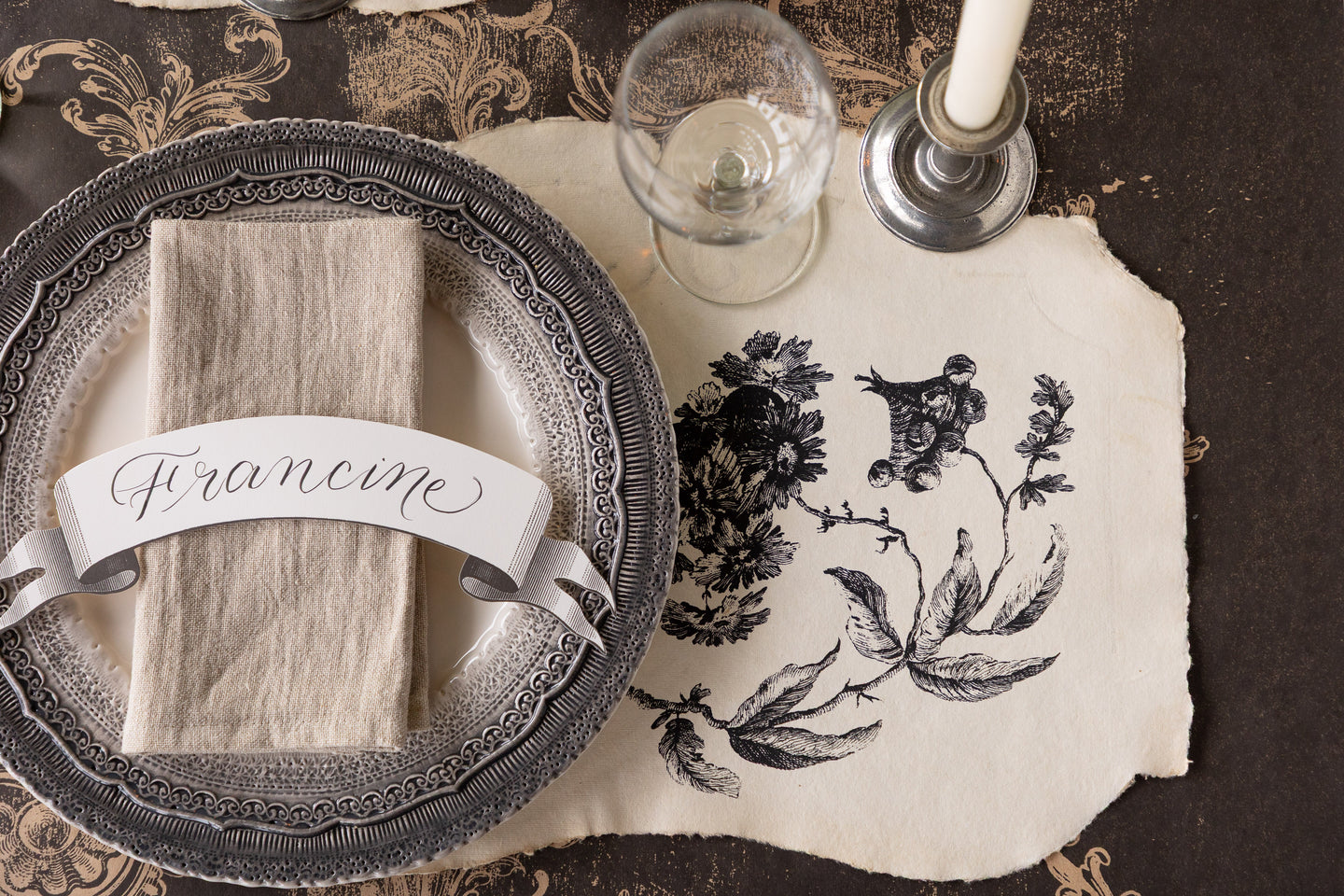 An elegant place setting featuring a Pillement Paper Placemat, decorative black dinnerware, Classic Black Banner Table Accent and candle on the Black Archival Runner. 