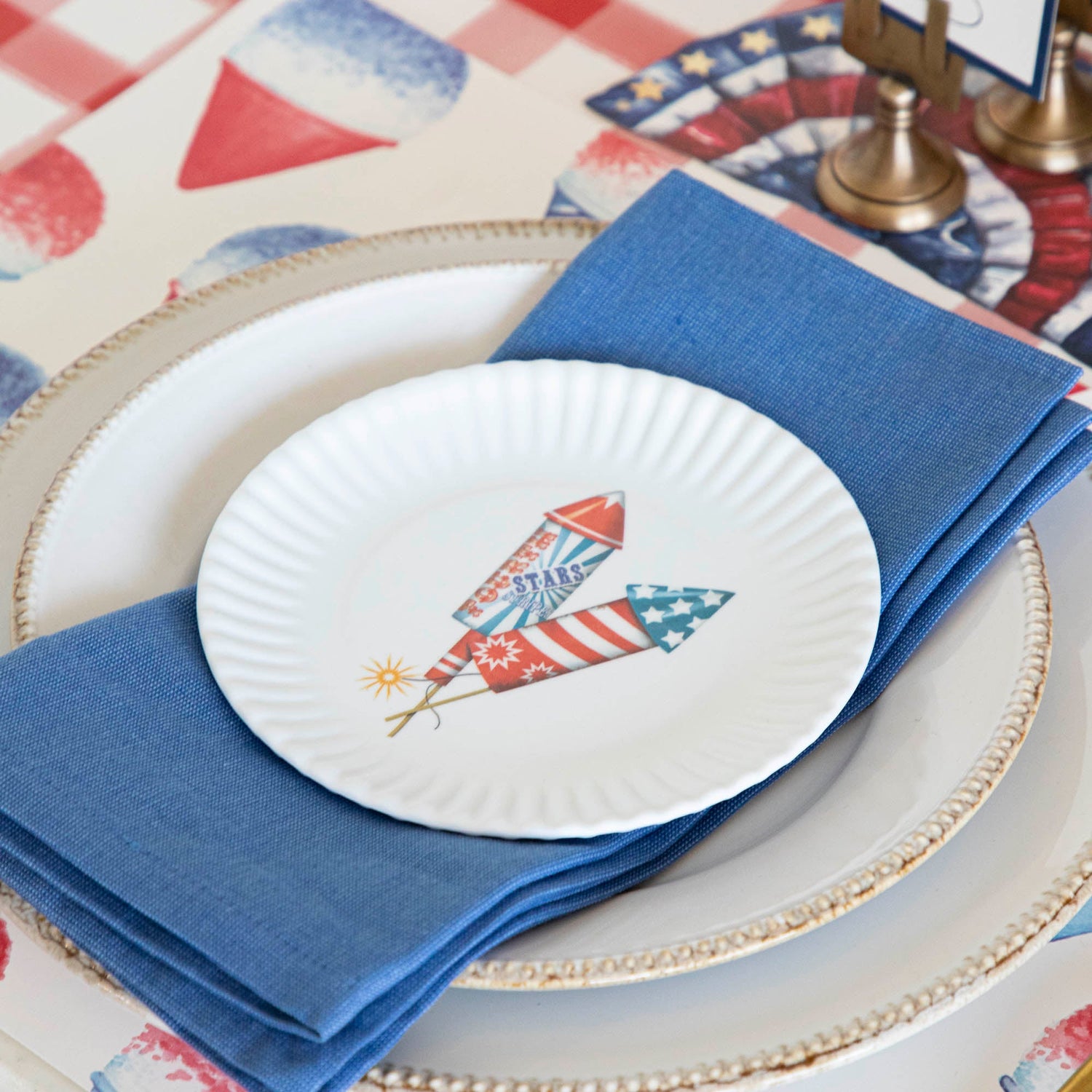 A patriotic place setting featuring the melamine american holiday plate, a blue napkin, white dinnerware and Snowcone Placemat.