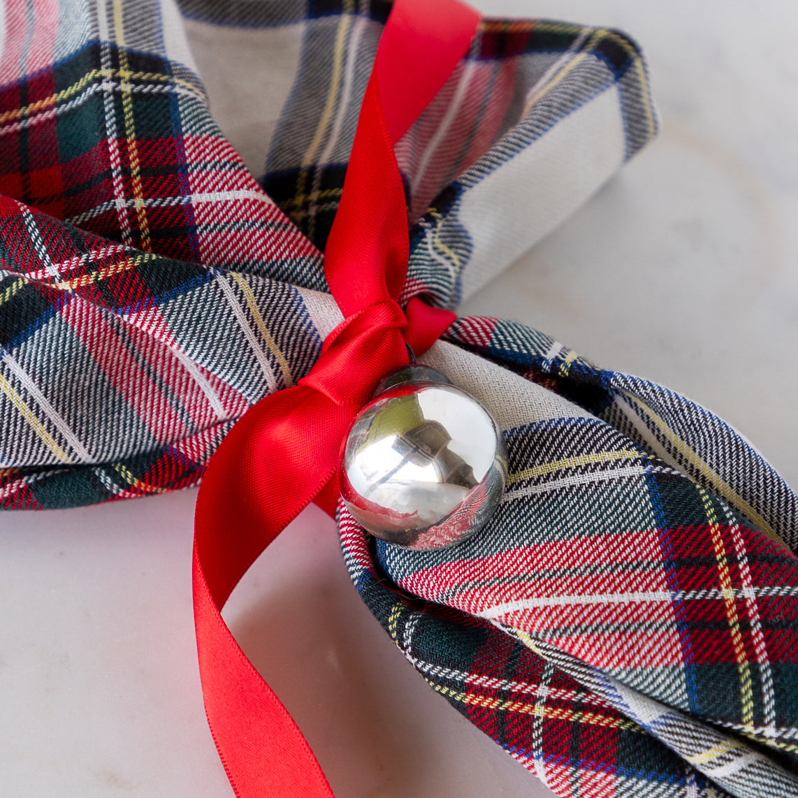 A Silver Ball Mercury Glass Ornament tied around a plaid napkin with a red ribbon.