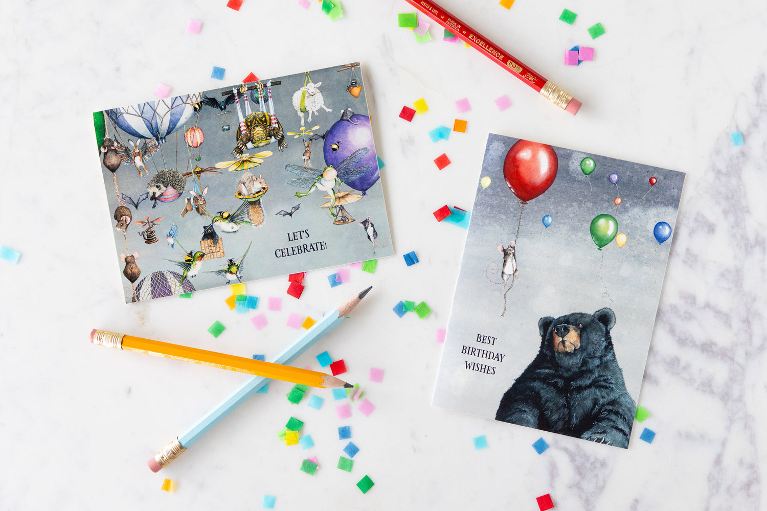 Two Maggie Vandewalle cards on a marble table surrounded by confetti and pencils.