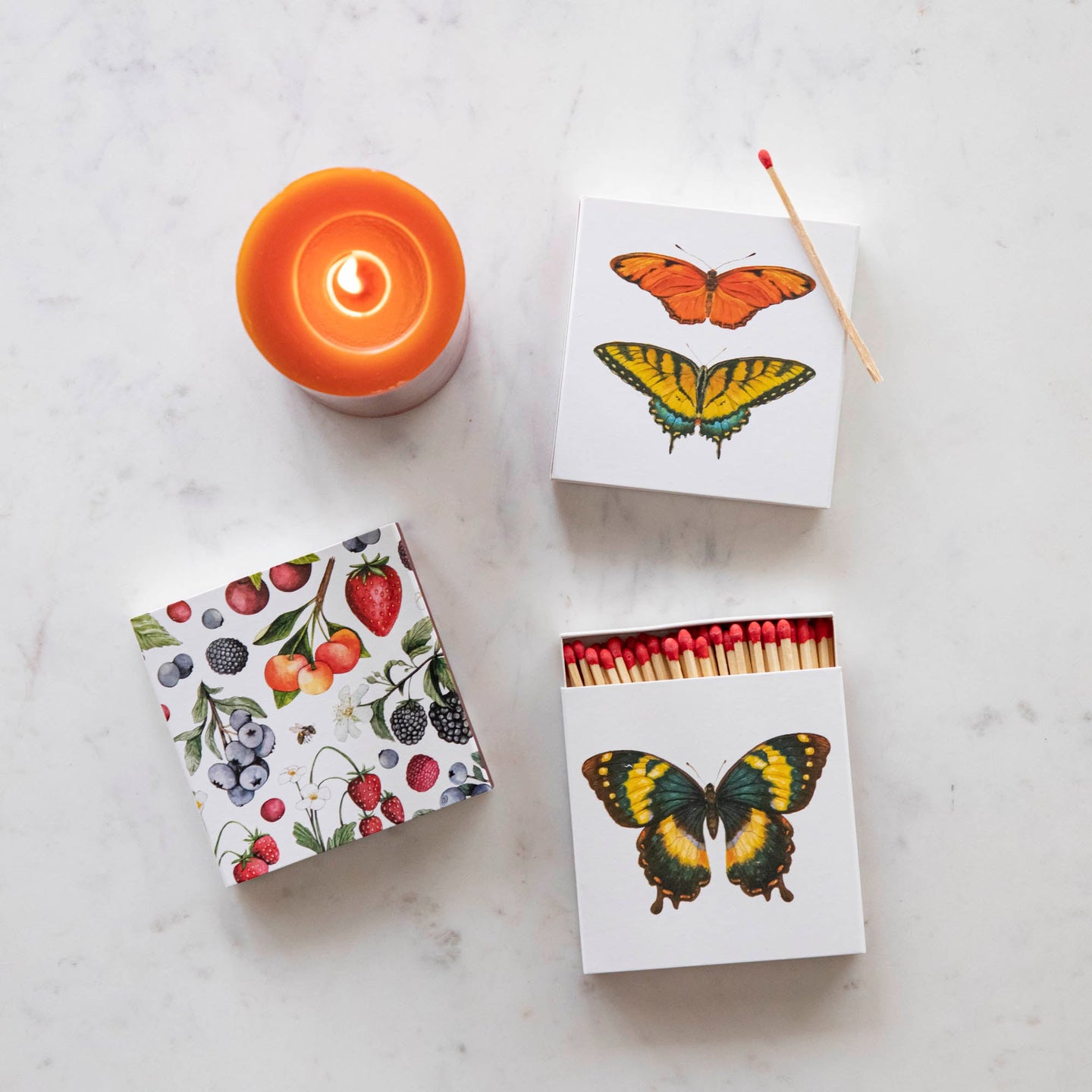 Wild Berry and Butterfly Matches on a table next to a burning candle.
