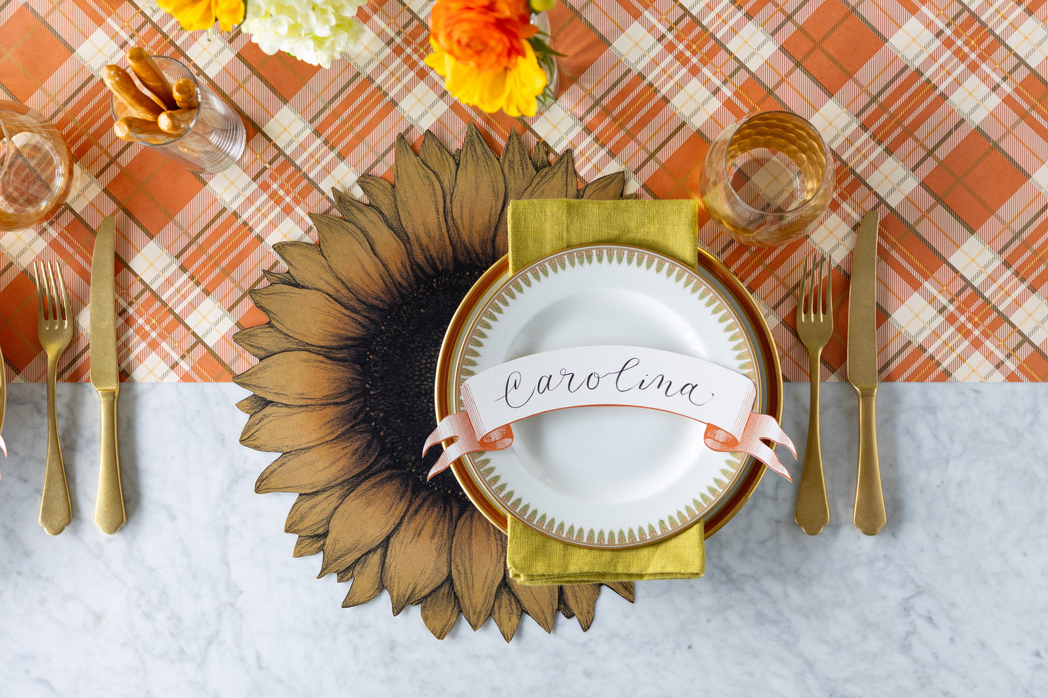 A fall table setting featuring the Die-cut Vintage Sunflower Placemat with vintage dinnerware, gold flatware and Classic Orange Banner Table Accent atop on the Orange Plaid Runner.