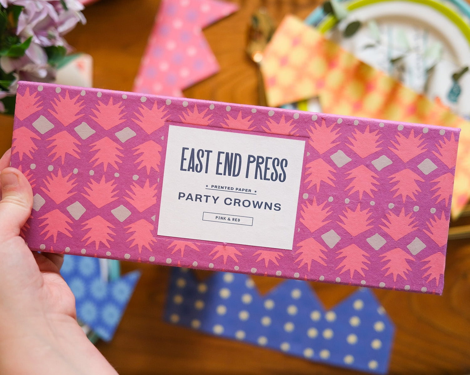 Box of East End Press party crowns with pink and red design on a wooden surface.