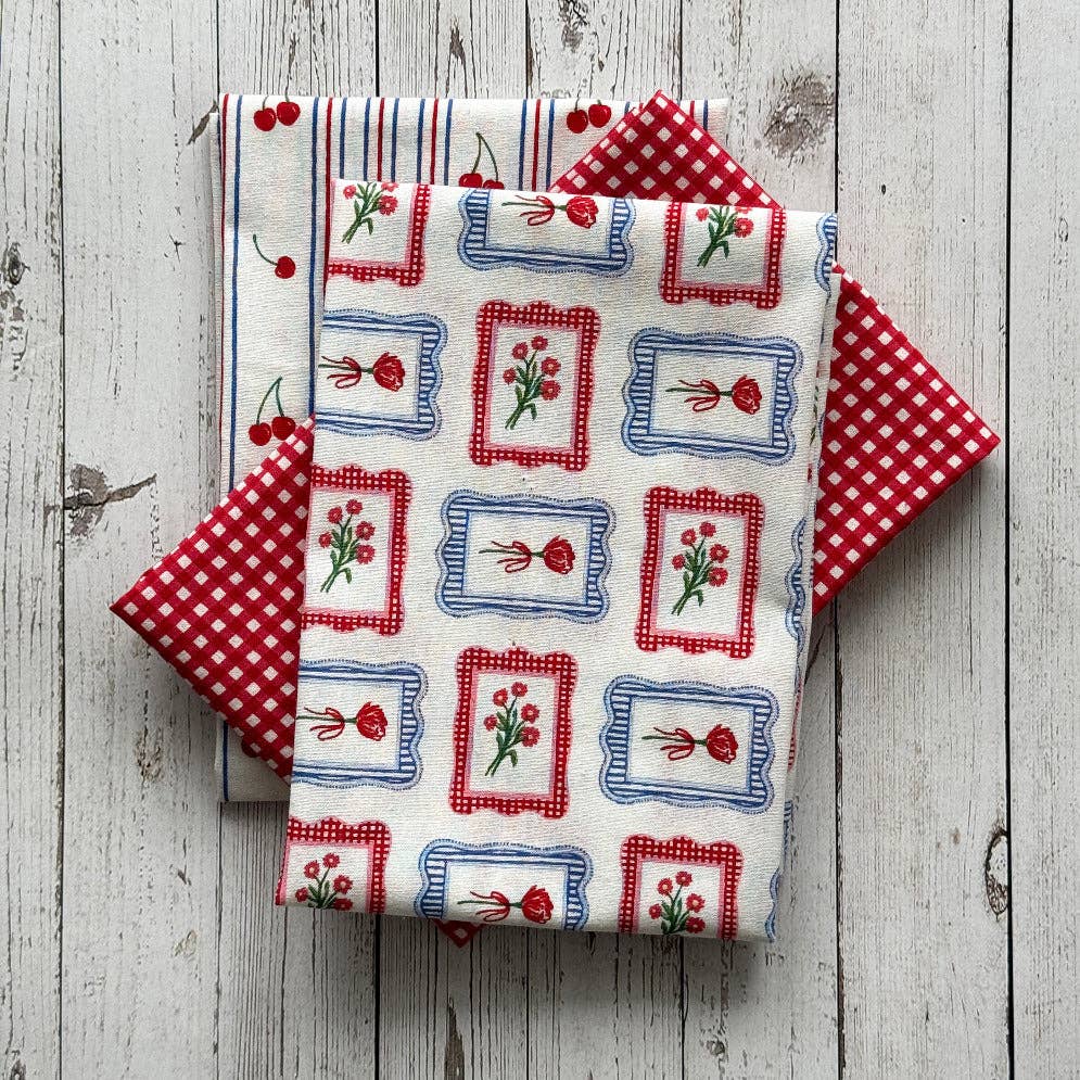 Collection of fabric tea towels with red, white, and blue patterns on a wooden surface.
