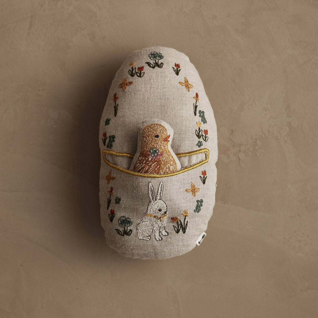Decorative egg with embroidered designs of a chick and rabbit on a beige background.