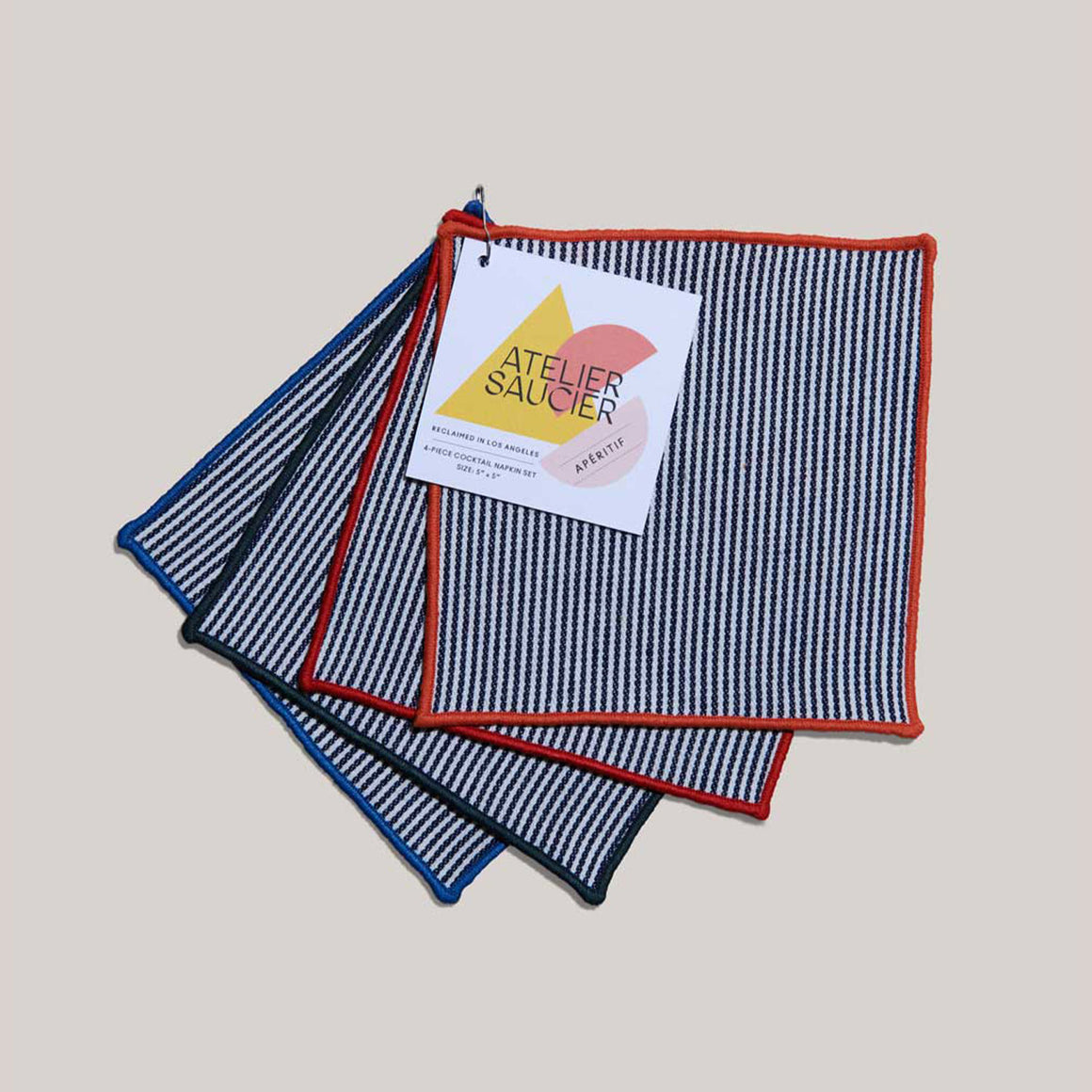Americana Stripe Napkin Set of 4 with a blue, green, red or orange trimming, and Atelier Saucier branded tag.