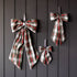 Three plaid fabric bows in red, green, black, and white tartan patterns, displayed on a dark gray vertical wood plank wall.