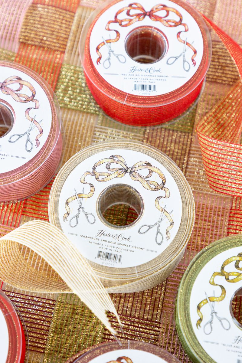 Several spools of sparkly ribbon in various colors unraveled on a surface of woven sparkle ribbon. 
