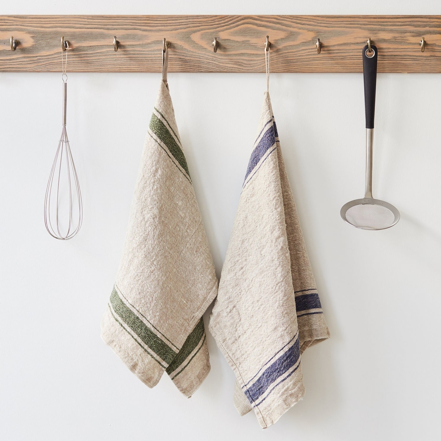 Two kitchen towels hanging on a wooden rack with utensils.