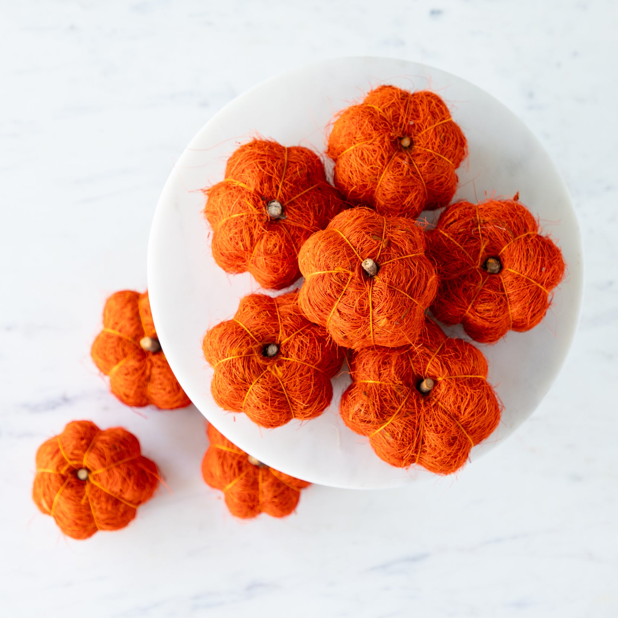 Burnt orange coco fiber pumpkins on a white cake stand with a wooden base against a green wall.