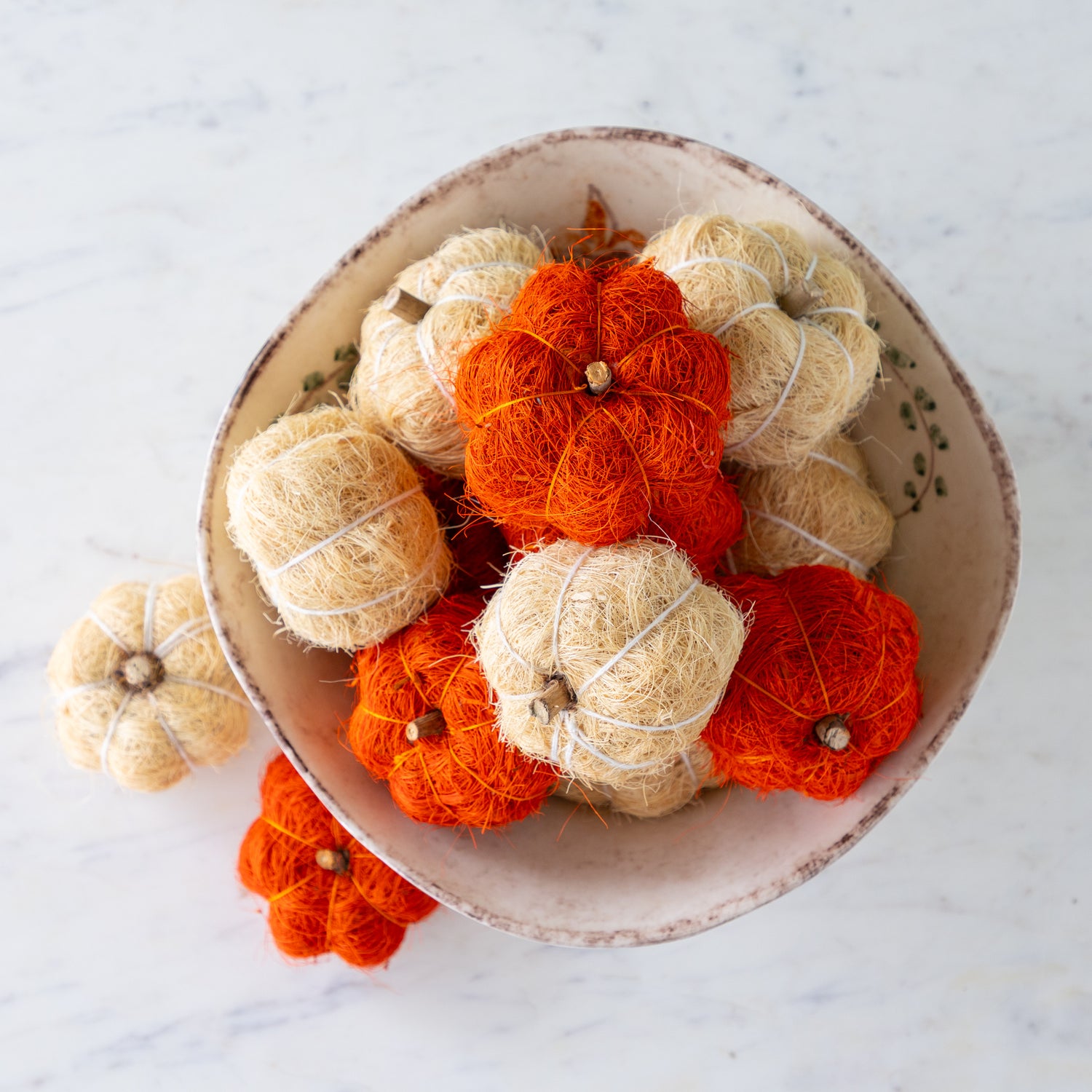 Coco fiber decorative pumpkins in burnt orange and cream in a bowl on a marble table.