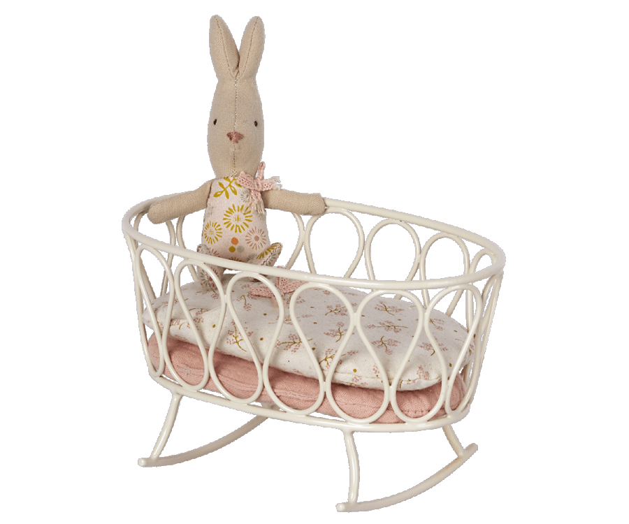 A Maileg stuffed rabbit toy resting on a white Maileg metal cradle against a wall with simple decor.