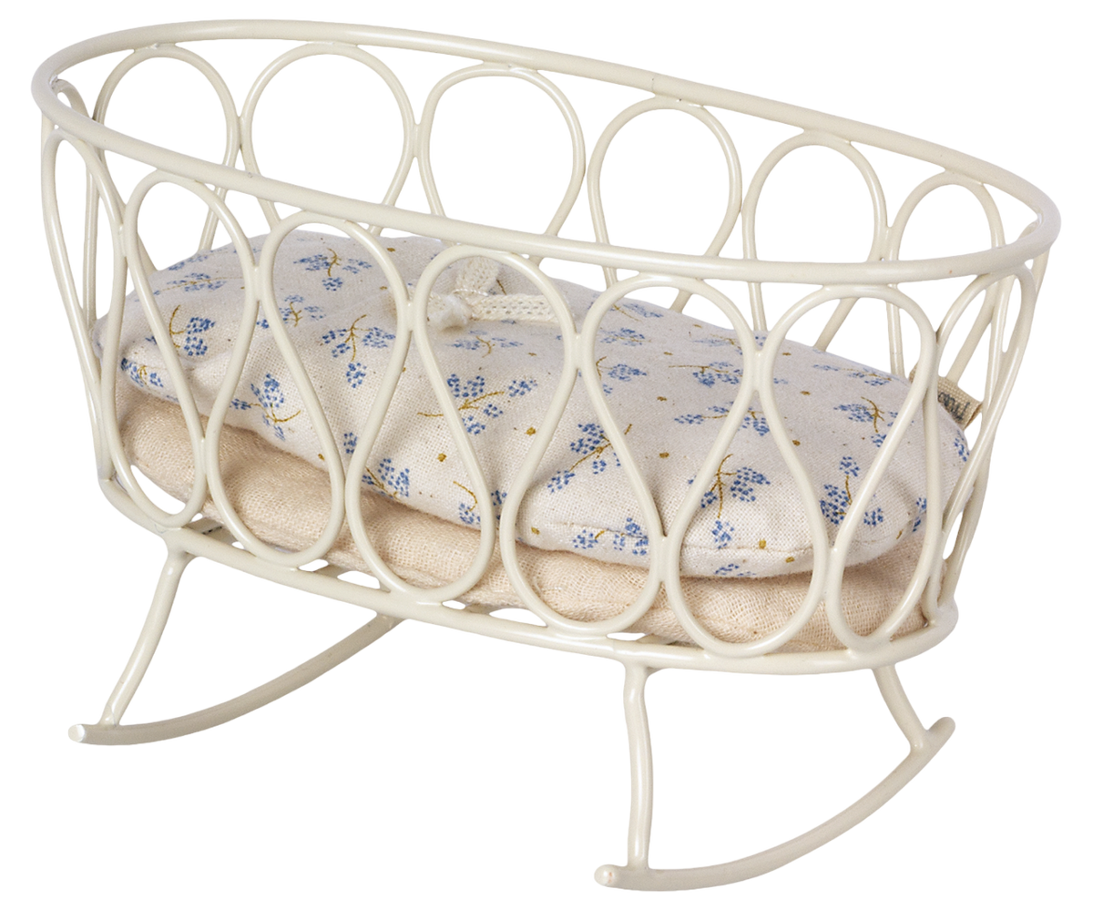 A Maileg stuffed rabbit toy resting on a white Maileg metal cradle against a wall with simple decor.