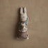Decorative rabbit plush toy with embroidered design on a beige background.