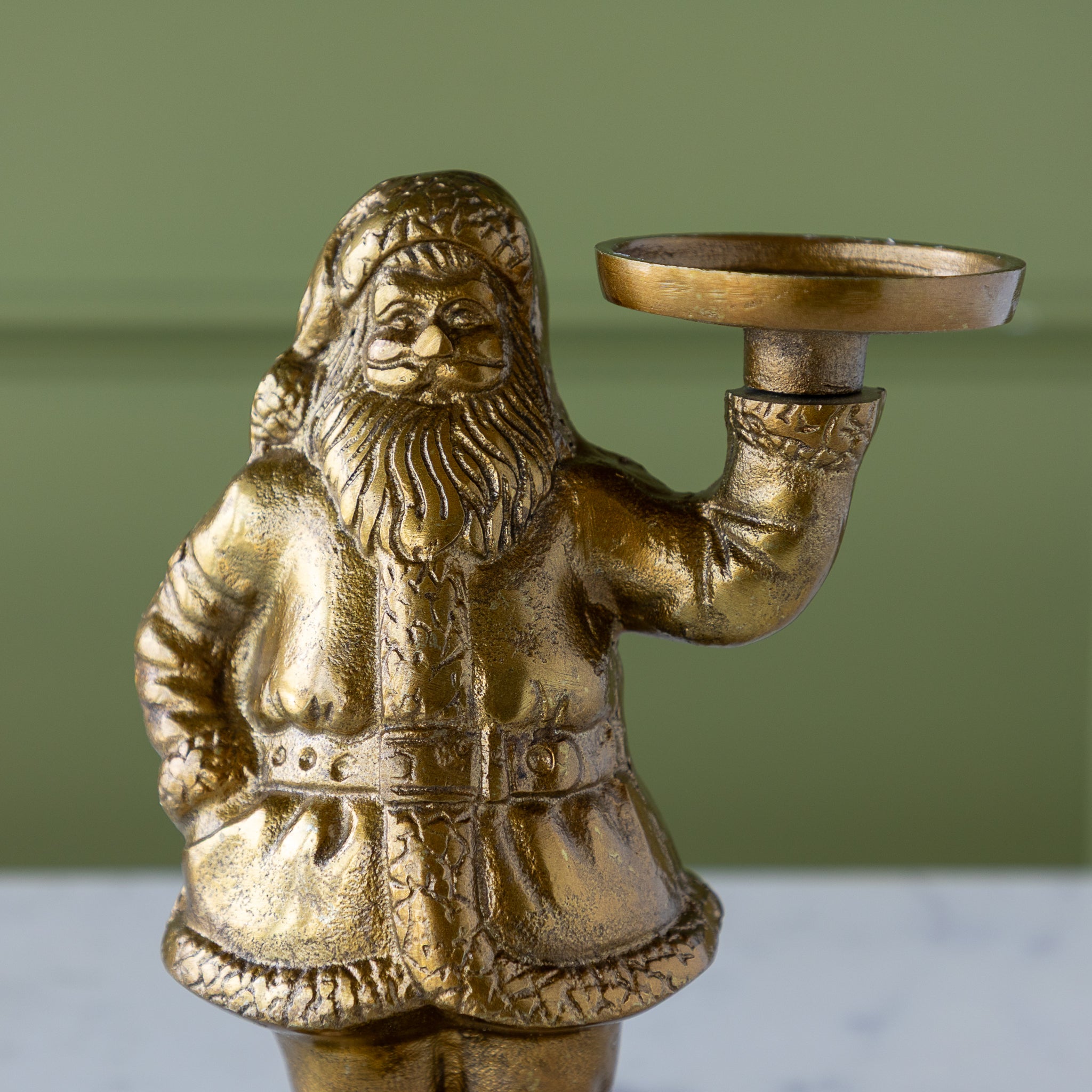 Gold Saint Nick Figurine holding a candle holder on a marble surface with a green wall background.