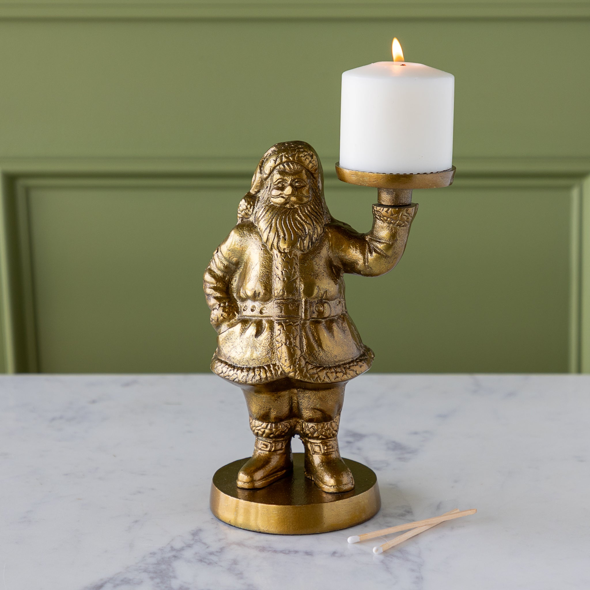Gold Saint Nick Figurine holding a pillar candle on a marble surface with a green wall background.