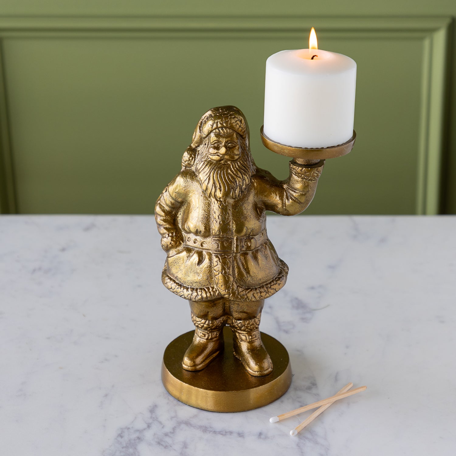 Gold Saint Nick Figurine holding a pillar candle on a marble surface with a green wall background.
