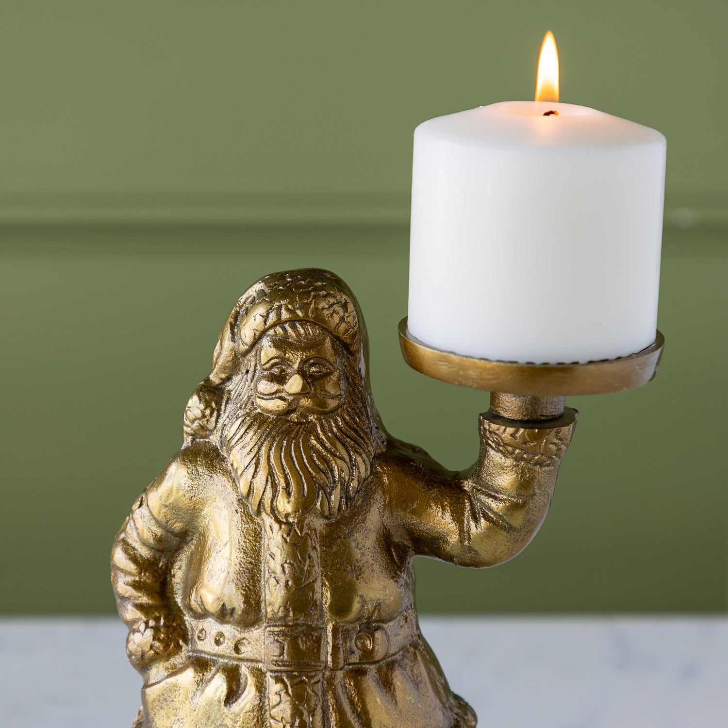 Gold Saint Nick Figurine holding a pillar candle on a marble surface with a green wall background.