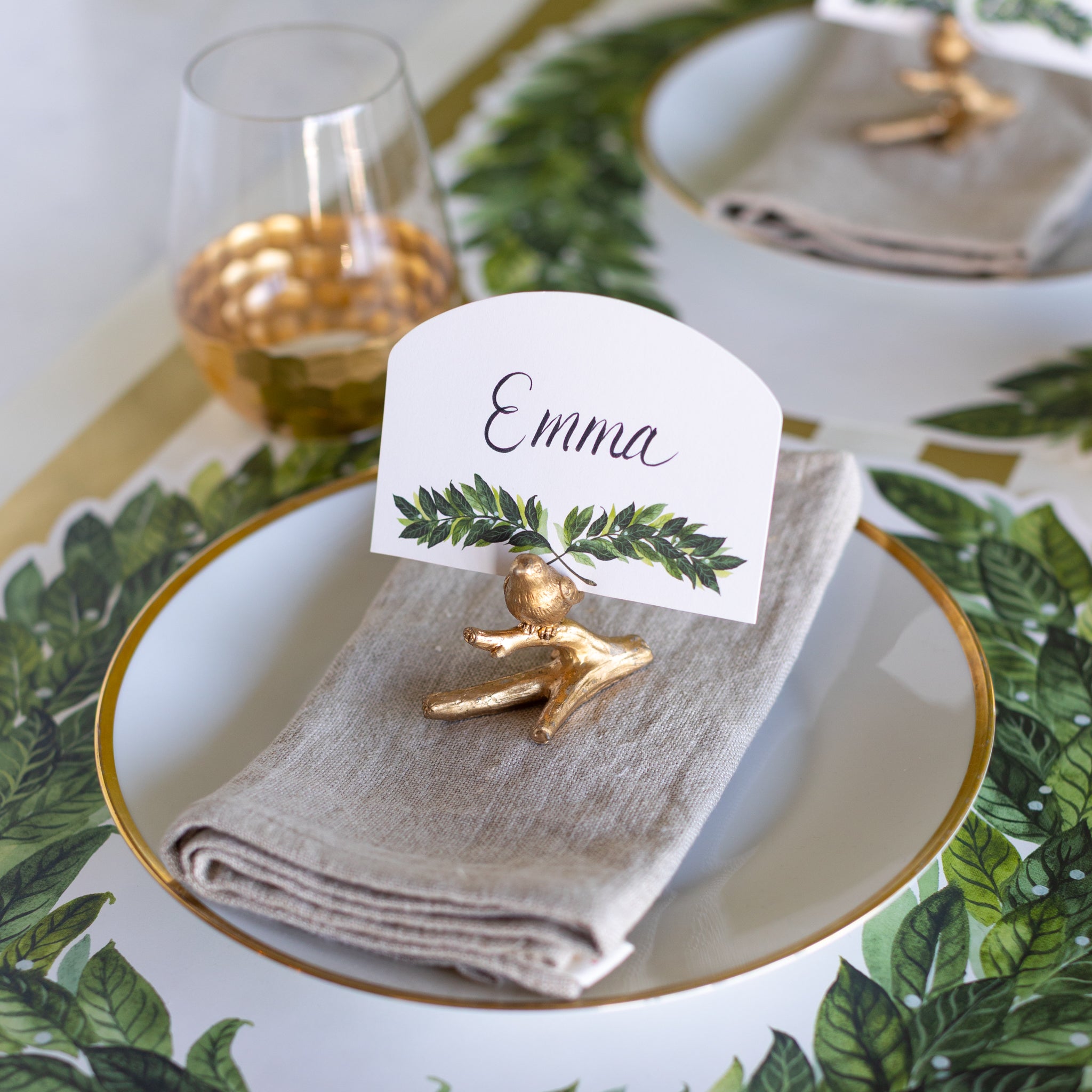 Table setting with a gold place card holder, folded napkin, and name card on the Die-cut Laurel Wreath Placemat.