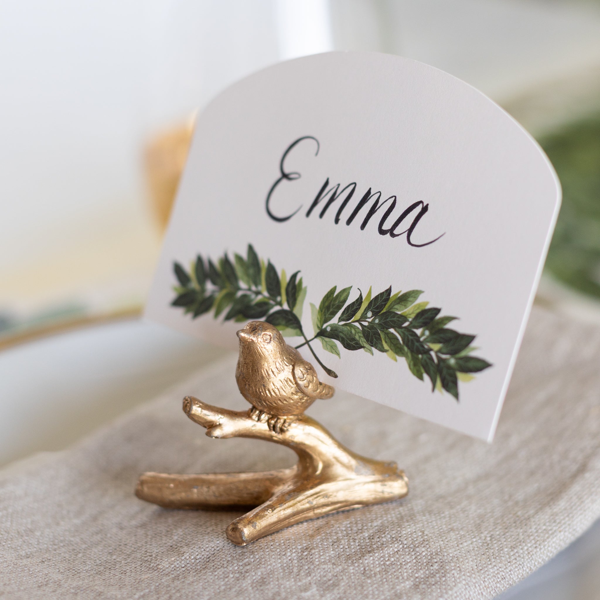 Gold bird-shaped place card holder with a name card featuring &