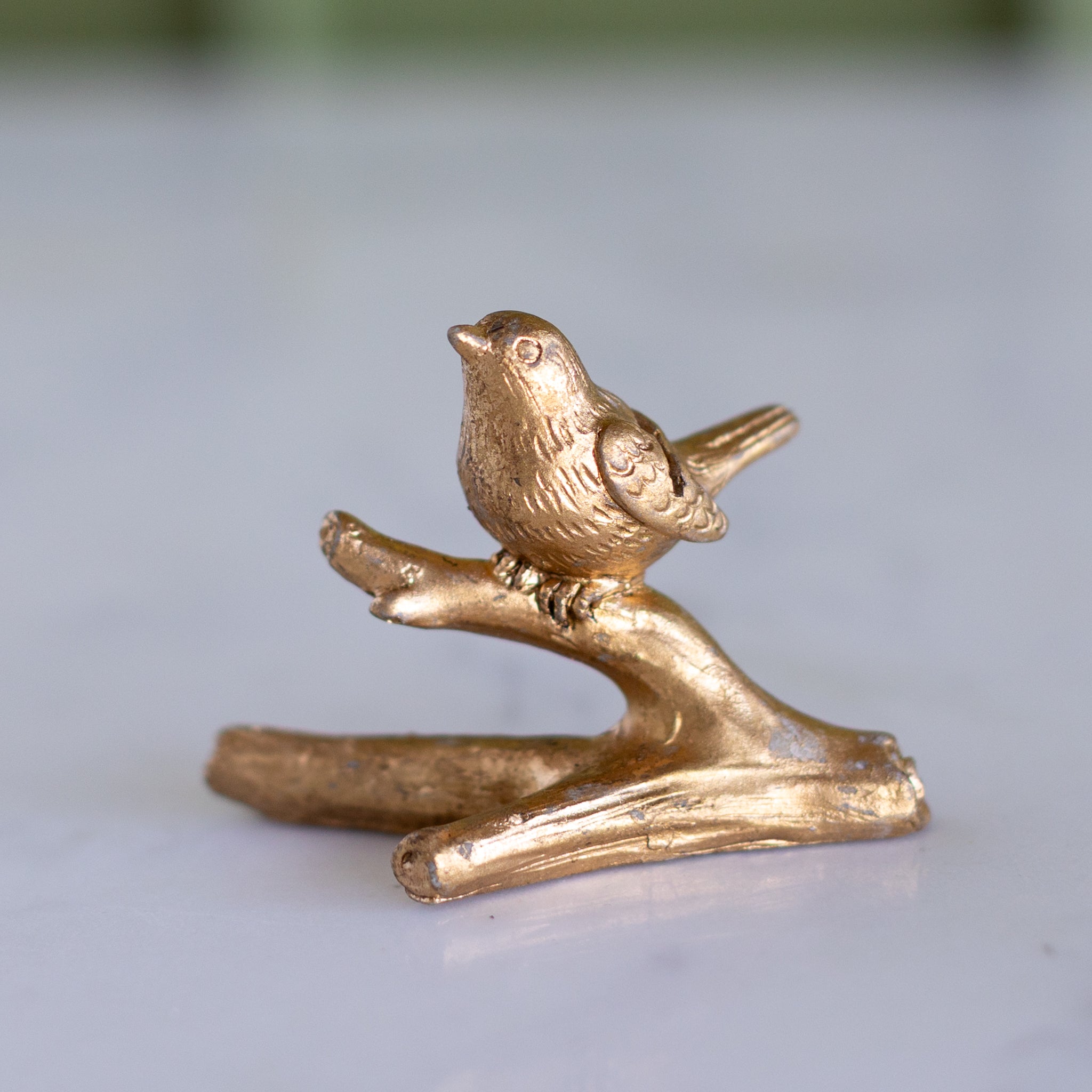 Bronze bird on a branch against a light background.