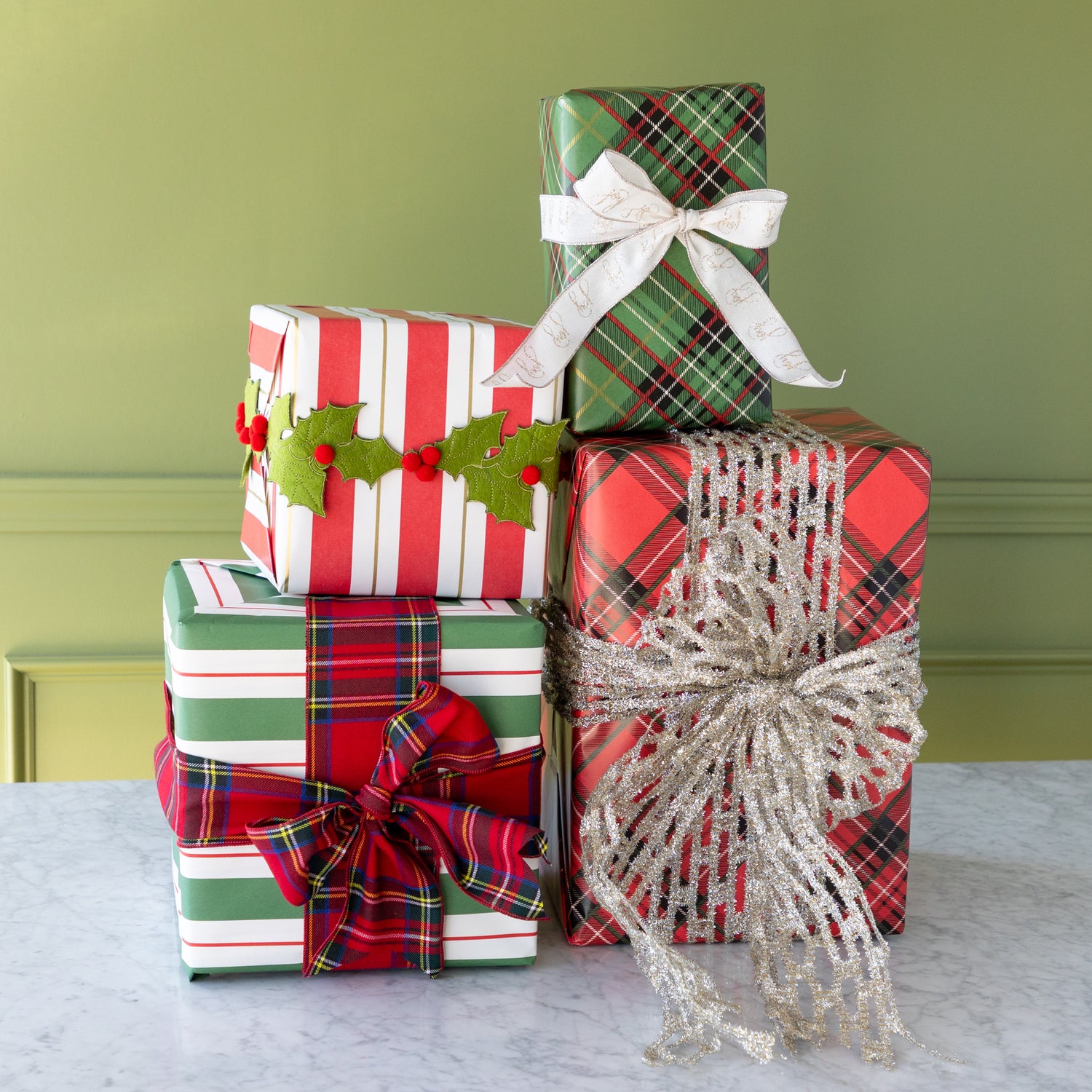 Stack of Christmas presents wrapped in plaid and striped paper with decorative bows on a marble surface.
