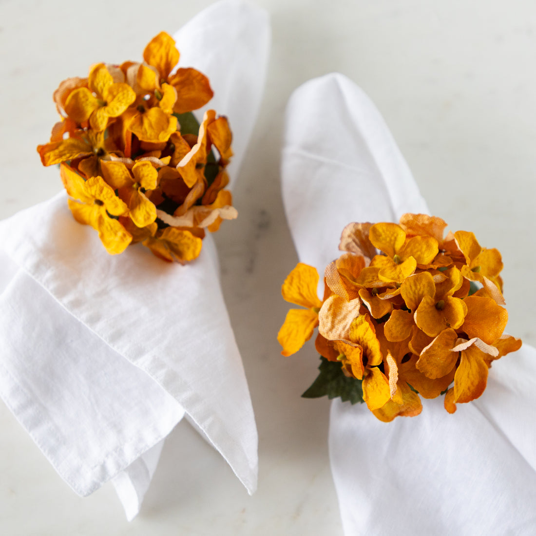 Two Fall Mustard Hydrangea Napkin Rings on white napkins against a light background.