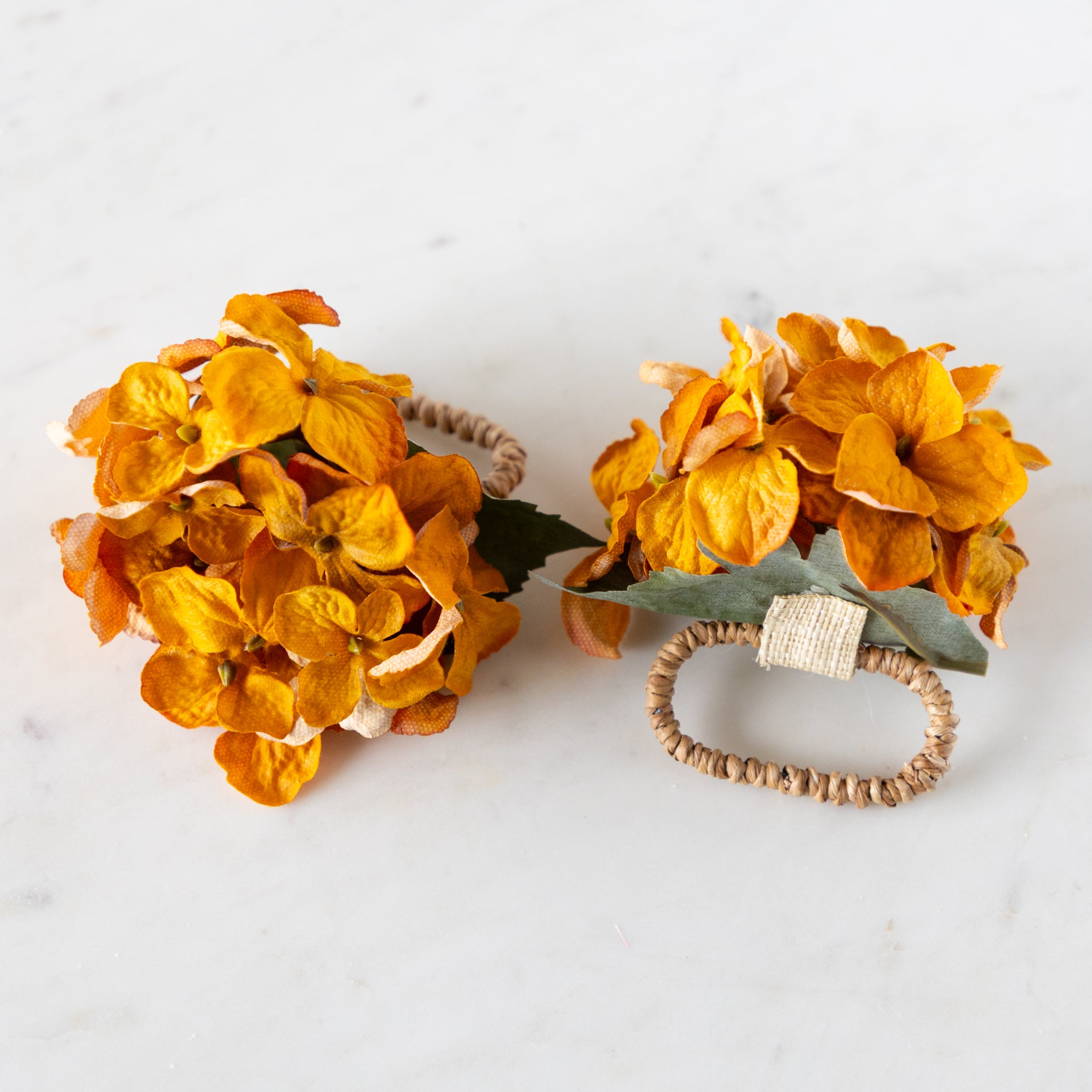 Two Fall Mustard Hydrangea Napkin Rings with rattan rings on a marble surface.